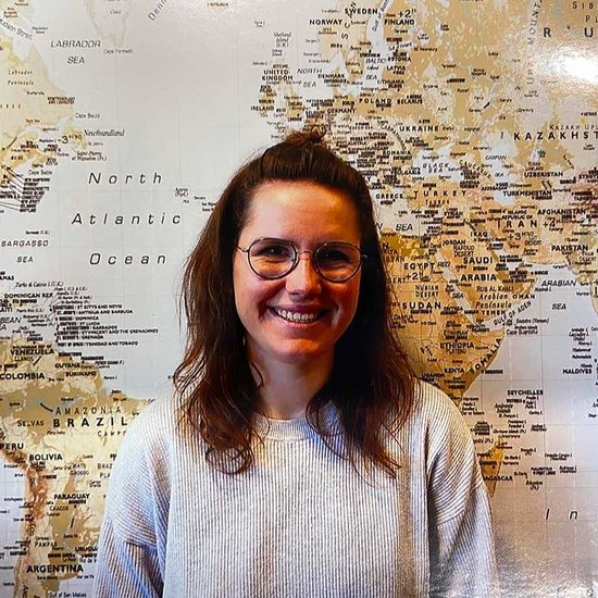 Eine Frau steht vor einer großen Weltkarte und lächelt in die Kamera
