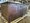 Ein großes, rustikales Sideboard aus dunklem Holz steht auf einer Palette in einer Werkstatt. Das Möbelstück hat Schranktüren und Schubladen mit schwarzen Metallgriffen.