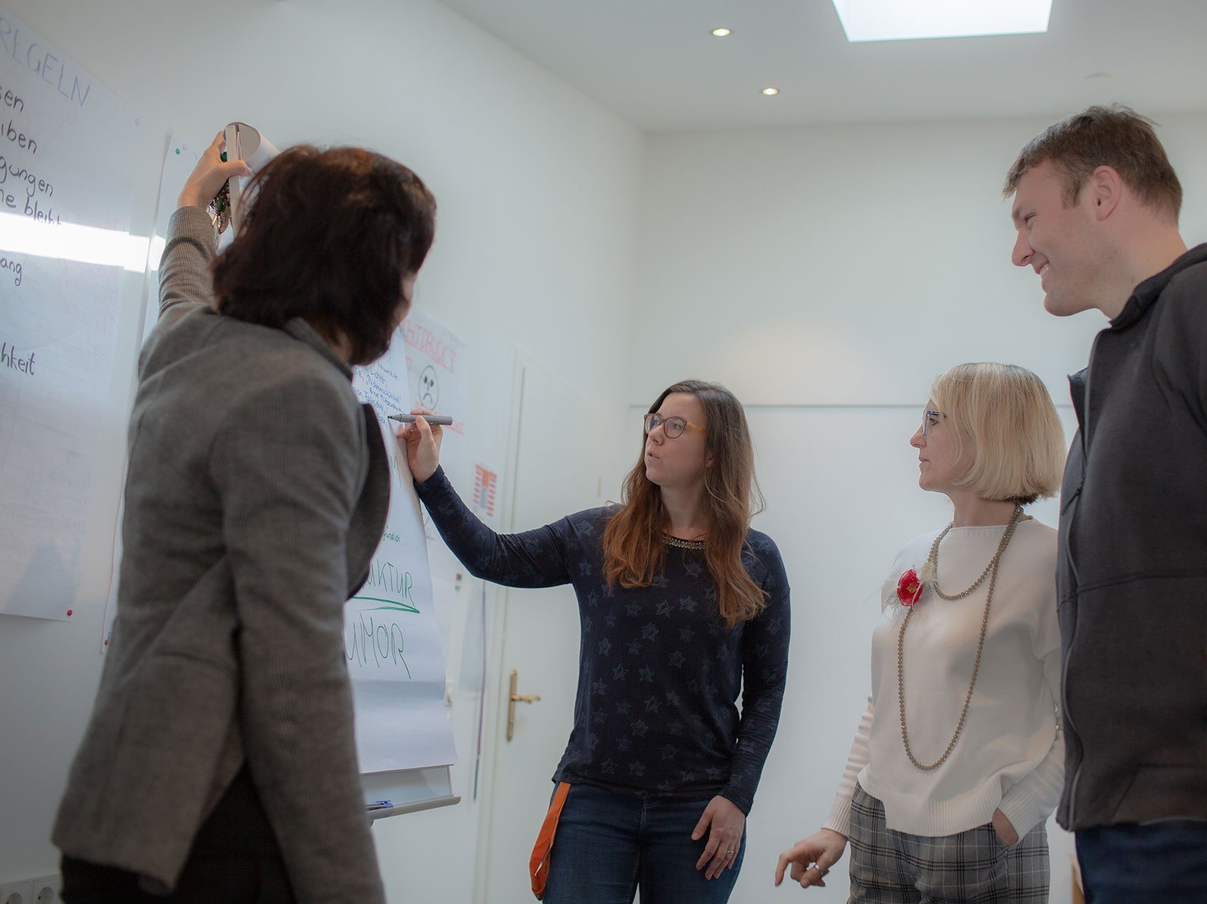 Eine Frau schreibt etwas auf ein Flipchart - zwei weitere Frauen und ein Mann sehen zu