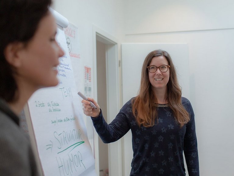 Eine Frau schreibt etwas auf ein Flipchart - zwei weitere Frauen und ein Mann sehen zu