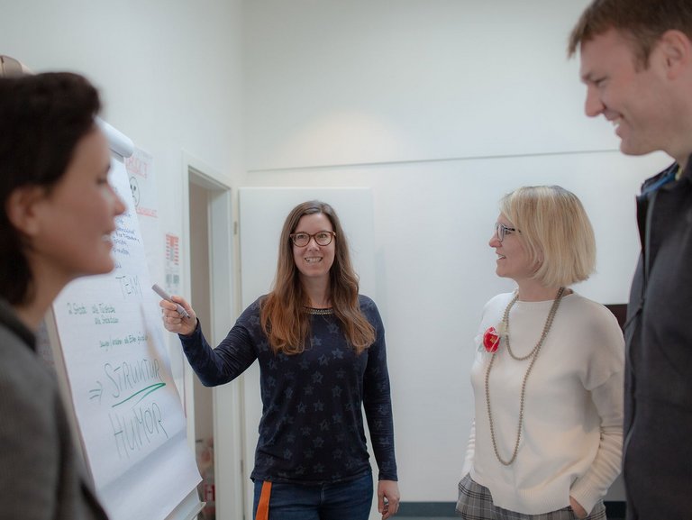 Eine Frau schreibt etwas auf ein Flipchart - zwei weitere Frauen und ein Mann sehen zu