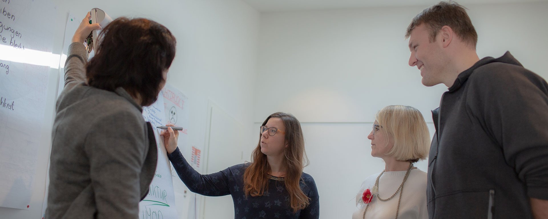 Eine Frau schreibt etwas auf ein Flipchart - zwei weitere Frauen und ein Mann sehen zu