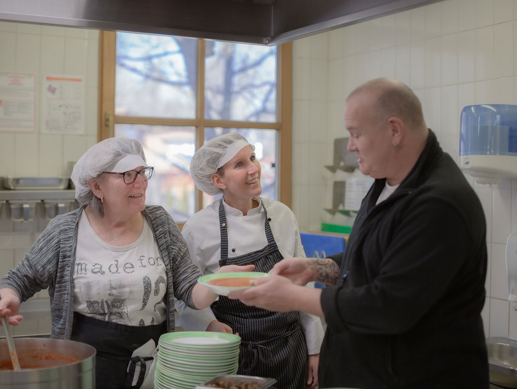 Zwei Köchinnen teilen Suppe in der Küche aus - ein Mann nimmt einen Teller